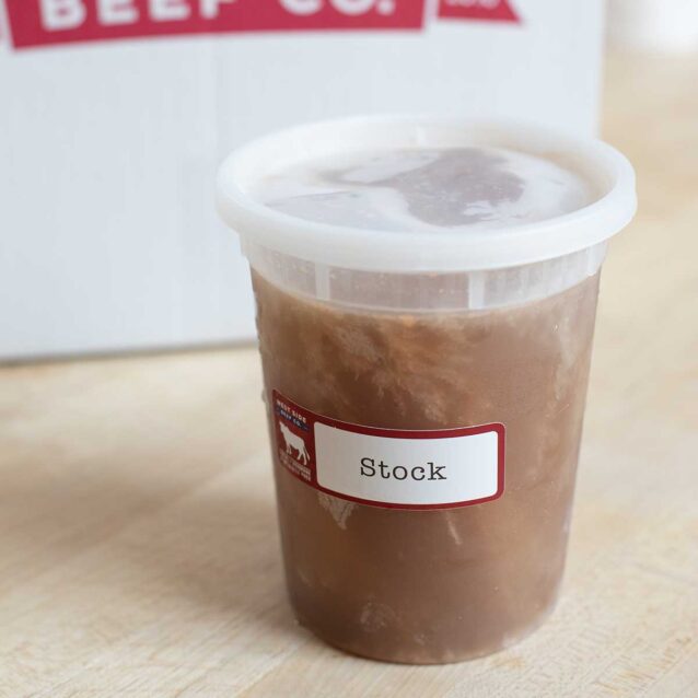 Container of beef stock in a clear plastic tub on a wooden surface