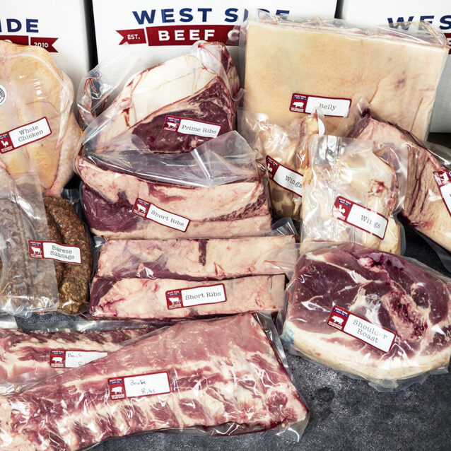 Assorted packaged meats, including whole chicken, ribs, pork belly, shoulder roast, sausages, and wings, arranged in branded boxes.