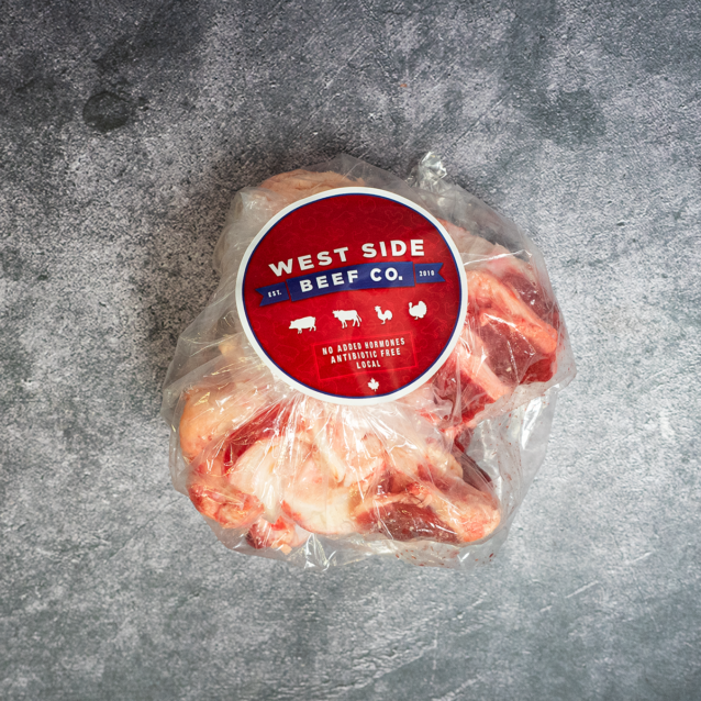A plastic bag of beef bones from West Side Beef Co. with a large branded label, placed on a gray textured surface.