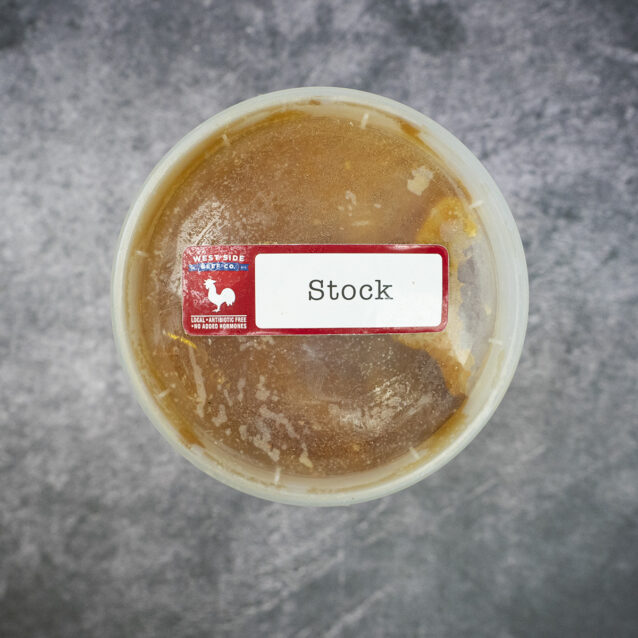Round plastic container of frozen chicken stock with a "Stock" label on a gray textured surface.