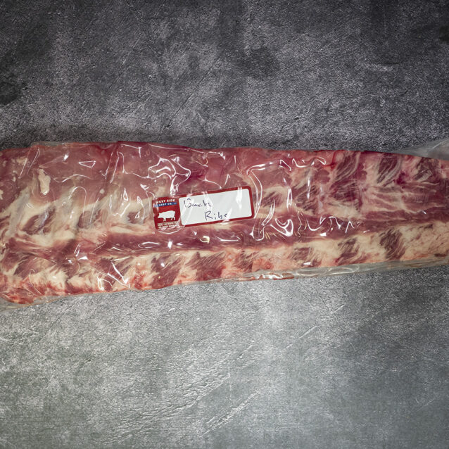 Vacuum-sealed rack of pork back ribs on a gray textured surface.
