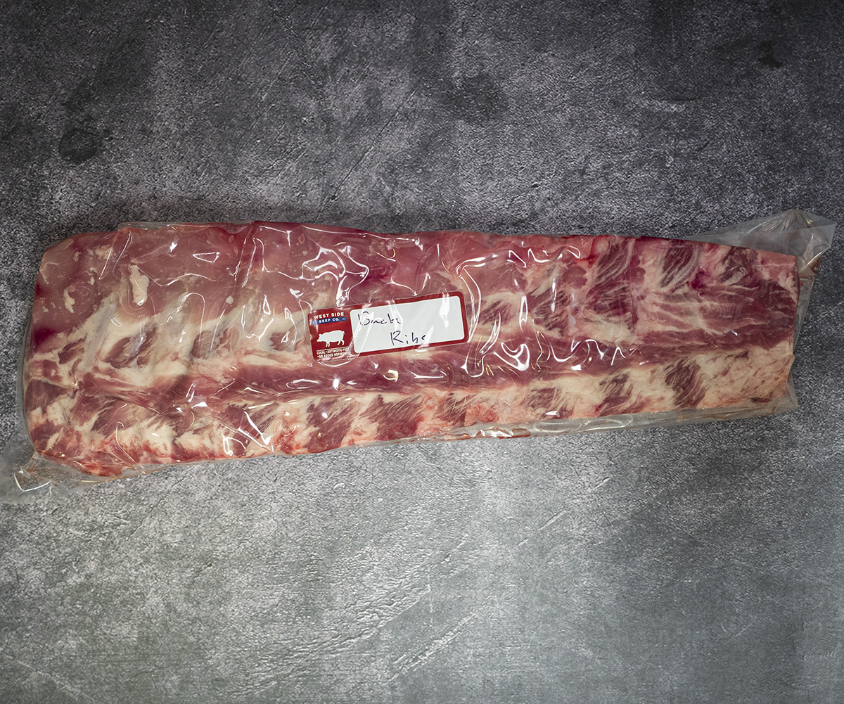 Vacuum-sealed rack of pork back ribs on a gray textured surface.