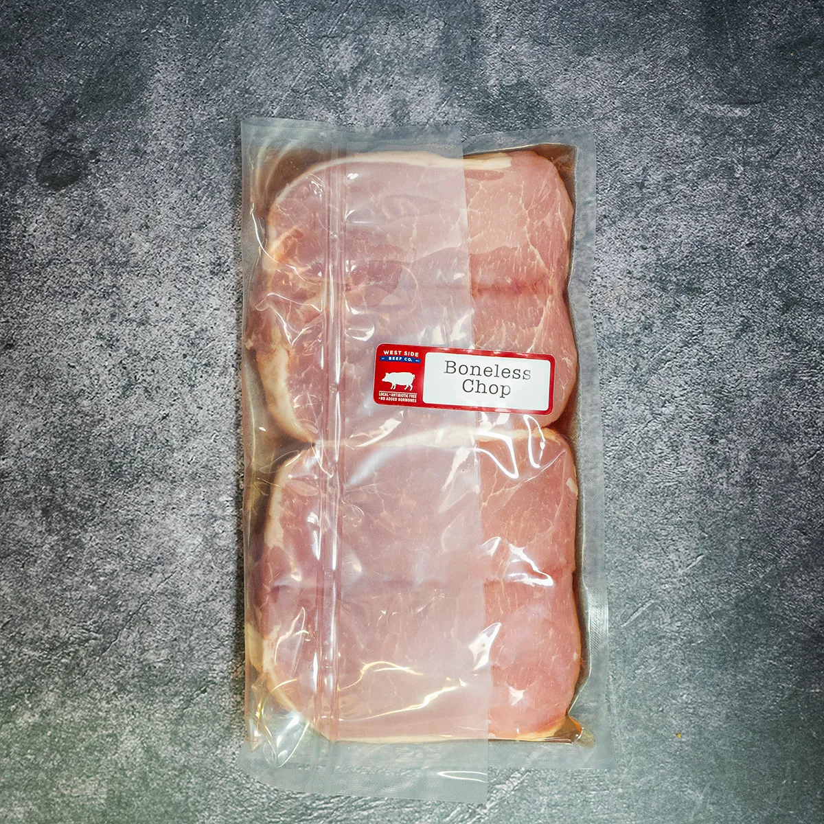A vacuum-sealed pack of boneless pork chops from West Side Beef Co. placed on a gray textured surface.