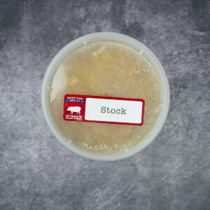 Round plastic container of frozen pork stock with a "Stock" label on a gray textured surface.