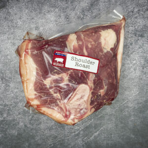 Vacuum-sealed bone-in pork shoulder roast with a "Shoulder Roast" label on a gray textured surface.