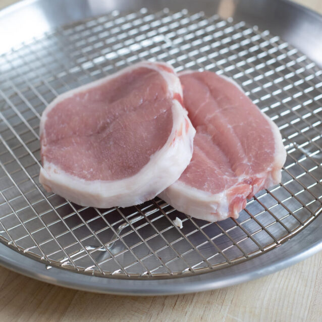 Raw pork loin chops on a wire rack over a metal tray.