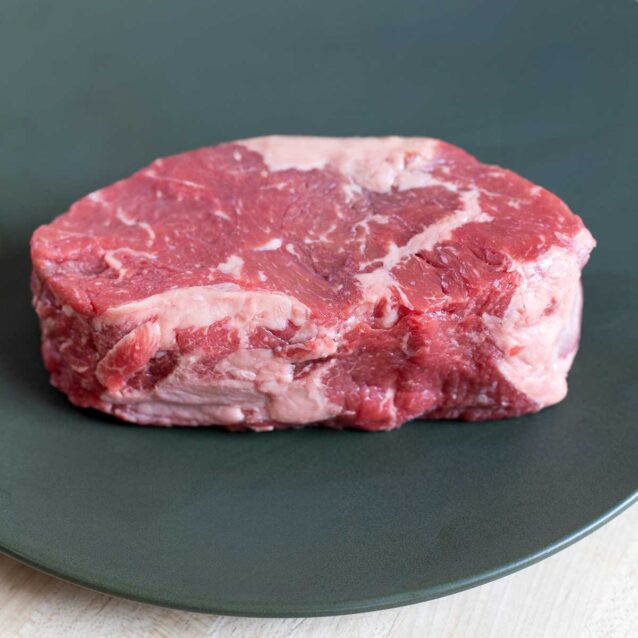 Thick-cut striploin steak with visible marbling and fat cap, placed on a dark plate.