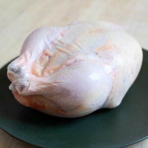 A whole raw chicken placed on a dark green plate on a wooden surface.