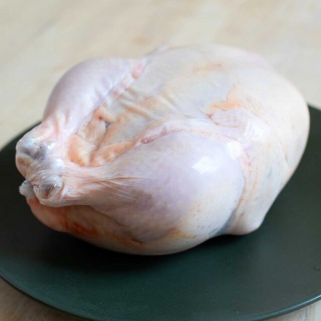 A whole raw chicken placed on a dark green plate on a wooden surface.