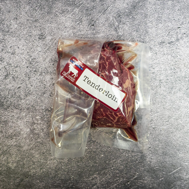 Vacuum-sealed beef tenderloin cut with label on a gray surface.