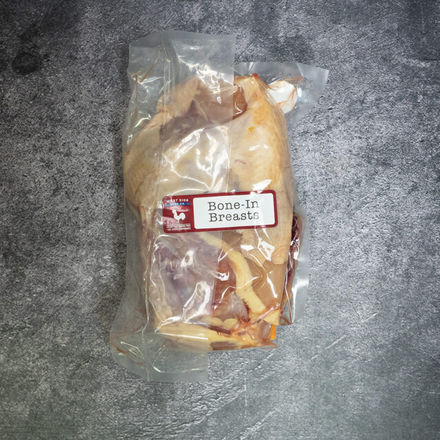Vacuum-sealed package of bone-in chicken breasts with skin on, labeled and placed on a gray surface.