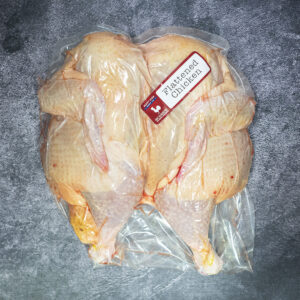 Whole flattened chicken vacuum sealed in plastic packaging on a textured surface.