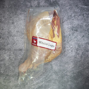 Whole chicken legs vacuum sealed in plastic packaging on a textured surface.