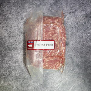 Vacuum-sealed package of ground pork, labeled and placed on a gray surface.