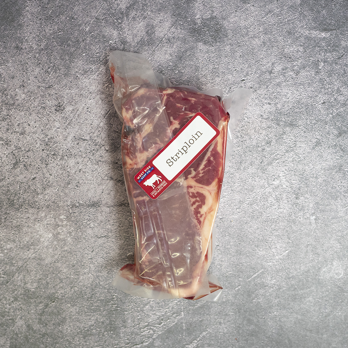 Vacuum-sealed thick-cut striploin steak, labeled and placed on a gray surface.