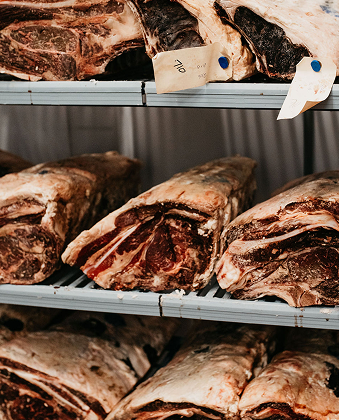 Cuts of beef stored on metal racks in a temperature-controlled room.