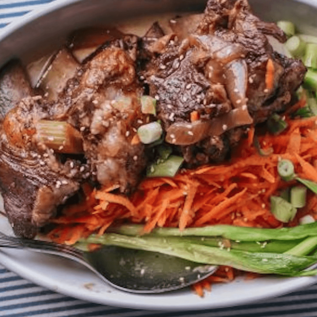 Braised short ribs served over shredded vegetables, topped with green onions and sauce.