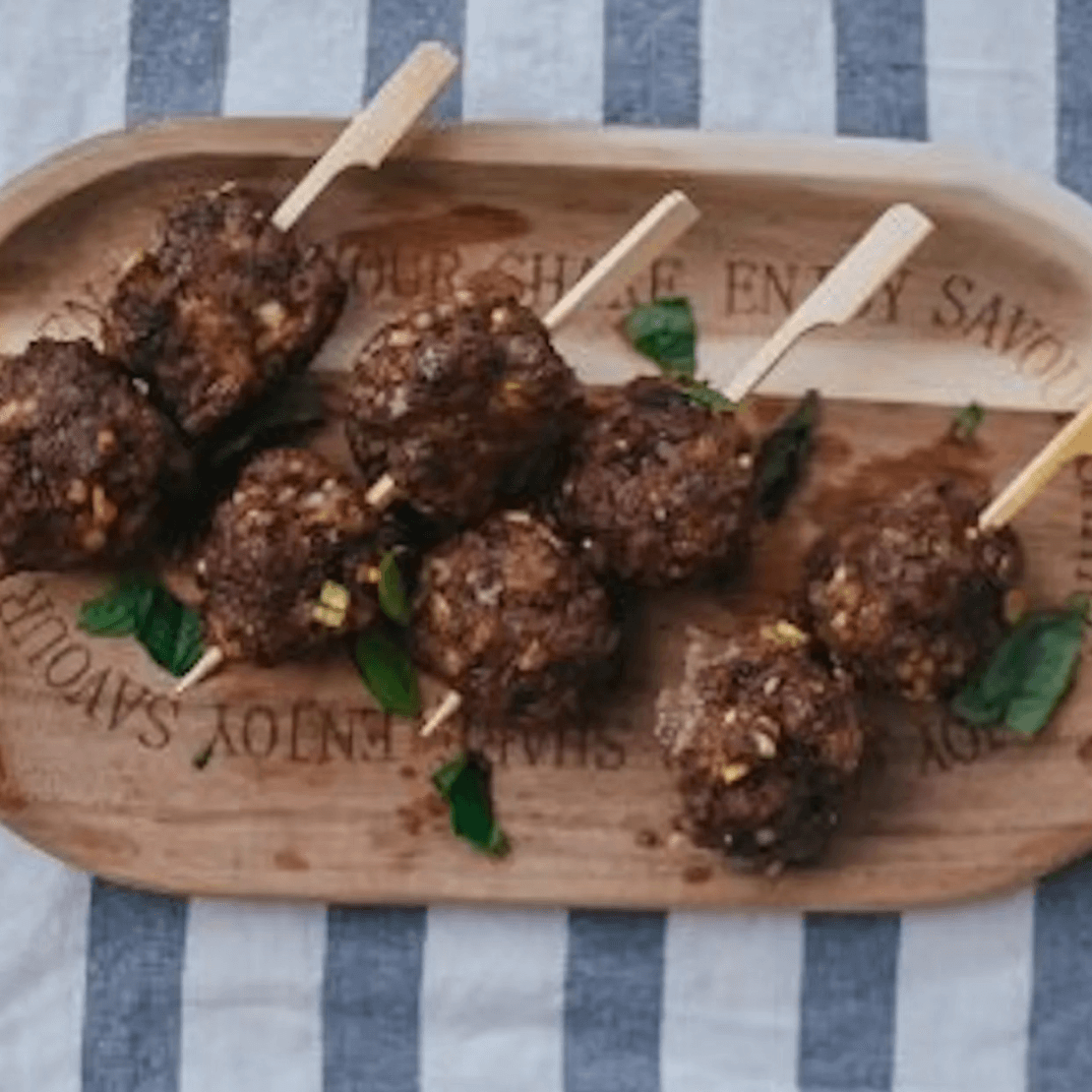 Cooked meatballs on skewers served on a wooden board with herbs.