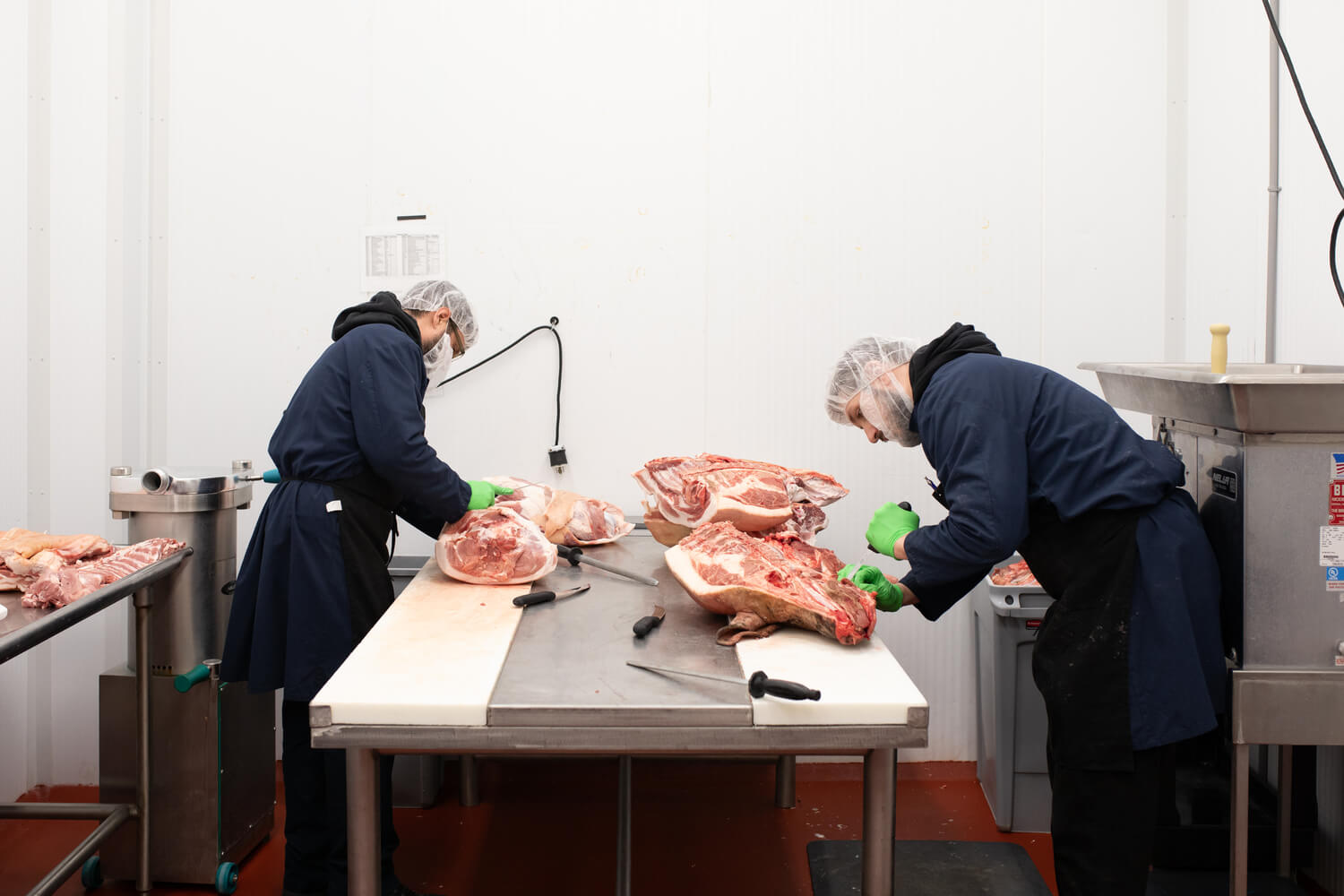 Butchers trimming large cuts of meat on a worktable in a processing room.