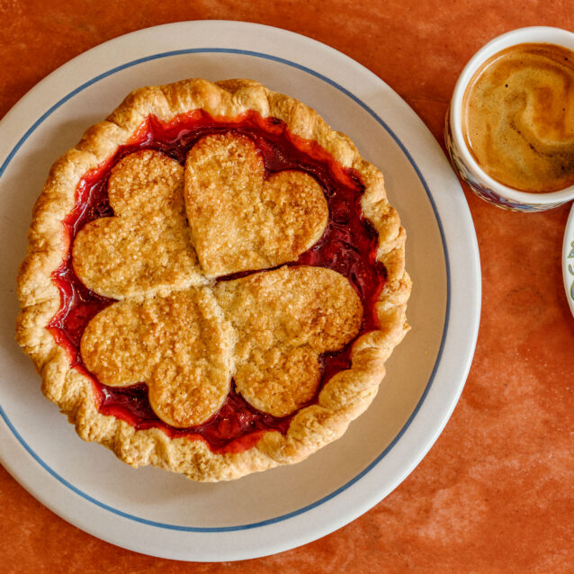 Sour cherry pie with heart-shaped crust design served on a plate with a cup of coffee.