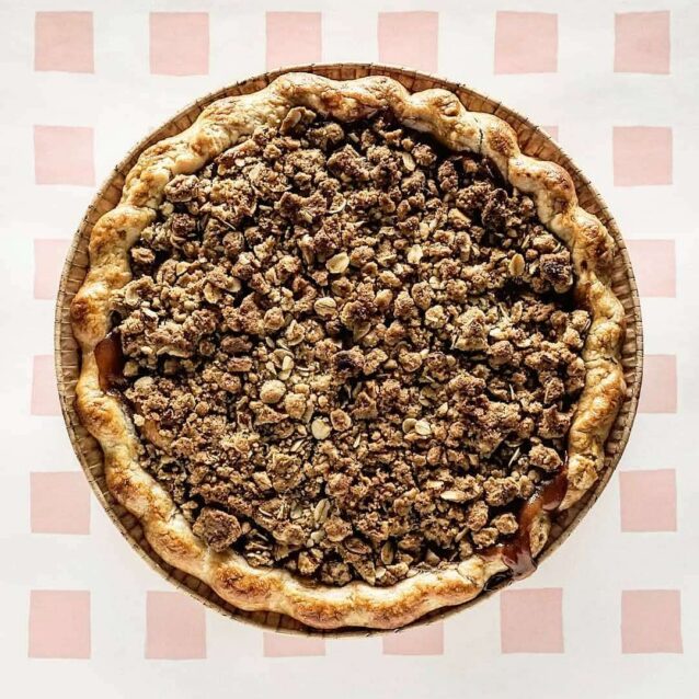 Whole apple crumble pie with oat topping on a patterned background.