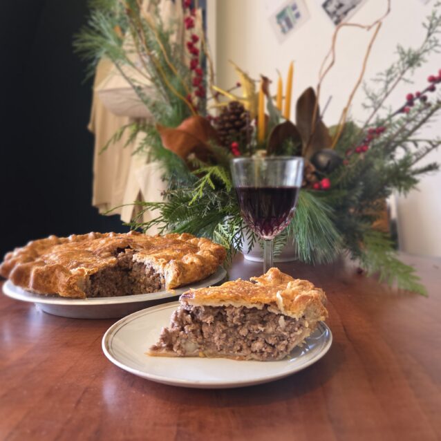 Slice of chicken pie on a plate with a whole pie in the background on a wooden table with seasonal decor.