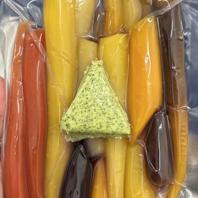 multi coloured carrots in a vac bag with a compound butter on top